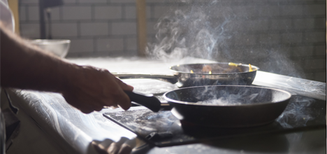 person using a stovetop with two hot sizzling frying pans on it