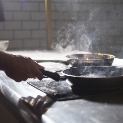 person using a stovetop with two hot sizzling frying pans on it