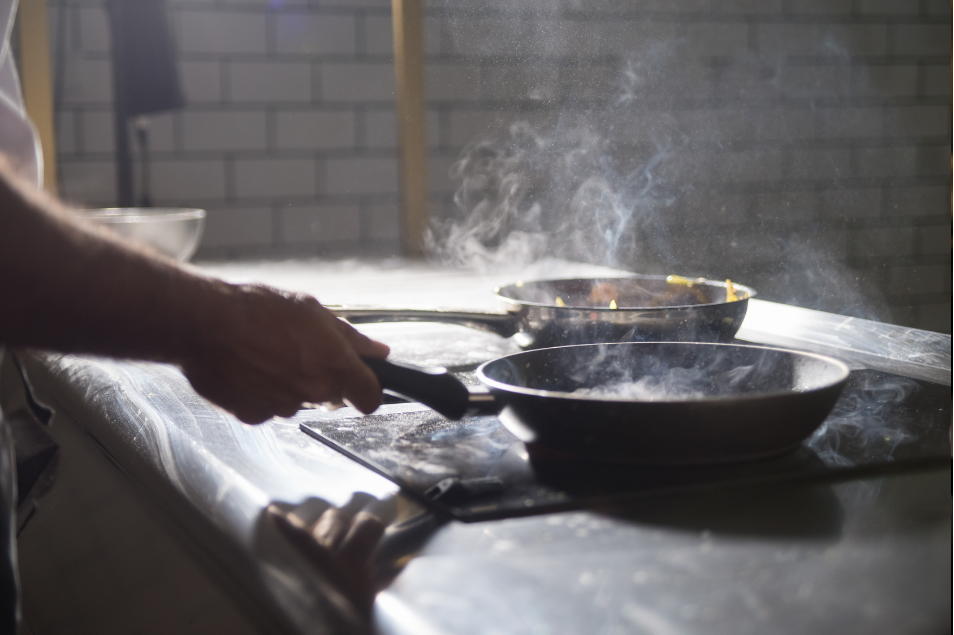 Close-up of person using a stove with two hot sizzling frying pans.